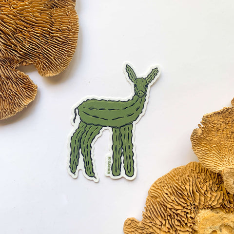 The Dill Doe Sticker featuring a female deer, aka doe, made out of dill pickles. The sticker is on a white background with dried mushroom decor.